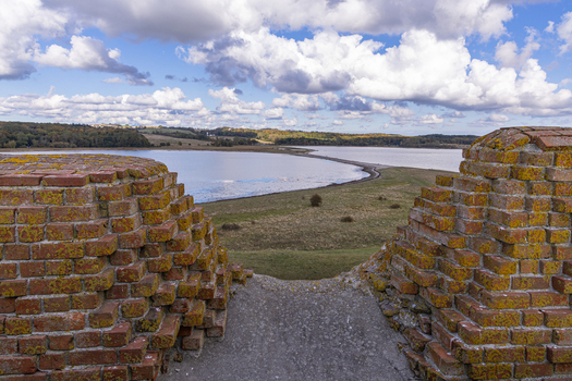 View of the historic brick ruins of Kalo Castle overlooking the calm waters of the bay and the surrounding landscape in Ronde Jutland Denmark. View of the historic brick ruins of Kalo Castle overlooking the calm waters of the bay and the surrounding landscape in Ronde Jutland Denmark.