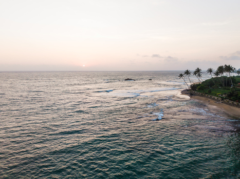 Aerial view of the tropical coastline with palm trees and ocean waves under a soft sunset sky Galle Southern Province Sri Lanka. Aerial view of the tropical coastline with palm trees and ocean waves under a soft sunset sky Galle Southern Province Sri Lanka.