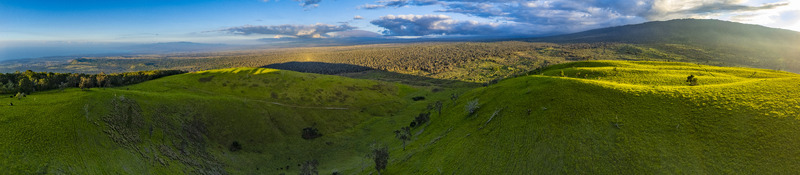 Aerial view of the Puu Waawaa cinder cone featuring lush green rolling hills and a vast volcanic landscape under a cloudy sky in Hawaii County Hawaii United States. Aerial view of the Puu Waawaa cinder cone featuring lush green rolling hills and a vast volcanic landscape under a cloudy sky in Hawaii County Hawaii United States.