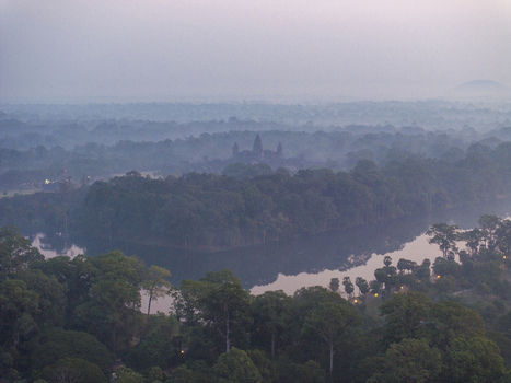 Aerial view of Angkor Wat temple towers rising above a dense green forest and a calm moat under a misty morning sky in Krong Siem Reap Siem Reap Province Cambodia. Aerial view of Angkor Wat temple towers rising above a dense green forest and a calm moat under a misty morning sky in Krong Siem Reap Siem Reap Province Cambodia.