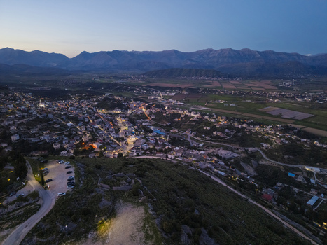 Aerial view of the coastal city of Saranda at dusk with glowing street lights and buildings nestled between mountains and fields in Saranda Vlore County Albania. Aerial view of the coastal city of Saranda at dusk with glowing street lights and buildings nestled between mountains and fields in Saranda Vlore County Albania.