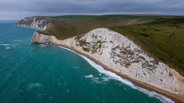 Aerial view of the limestone arch of Durdle Door featuring dramatic white chalk cliffs turquoise waters and rolling green hills along the Jurassic Coast in Wareham England United Kingdom. Aerial view of the limestone arch of Durdle Door featuring dramatic white chalk cliffs turquoise waters and rolling green hills along the Jurassic Coast in Wareham England United Kingdom.