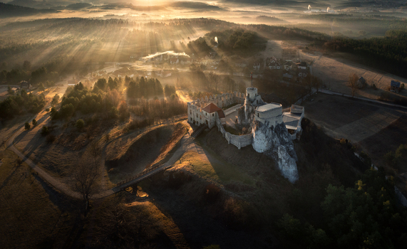 Aerial view of the medieval castle ruins on the Krakow Czestochowa Upland surrounded by misty forests and golden sun rays at sunrise Krakow County Lesser Poland Voivodeship Poland. Aerial view of the medieval castle ruins on the Krakow Czestochowa Upland surrounded by misty forests and golden sun rays at sunrise Krakow County Lesser Poland Voivodeship Poland.