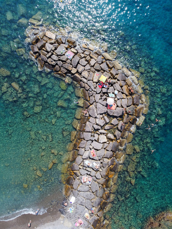 Aerial view of a stone breakwater with people sunbathing and swimming in the turquoise Mediterranean sea in Imperia Liguria Italy. Aerial view of a stone breakwater with people sunbathing and swimming in the turquoise Mediterranean sea in Imperia Liguria Italy.