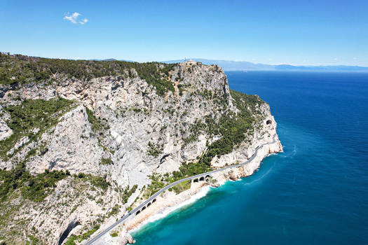 Aerial view of Promontorio di Varigotti featuring steep limestone cliffs and a coastal road along the turquoise Mediterranean Sea in Varigotti Liguria Italy. Aerial view of Promontorio di Varigotti featuring steep limestone cliffs and a coastal road along the turquoise Mediterranean Sea in Varigotti Liguria Italy.