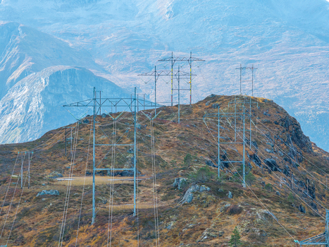 Aerial view of high voltage power lines crossing a rugged mountain ridge with autumn colored vegetation and dramatic peaks in the background Andalsnes More og Romsdal Norway. Aerial view of high voltage power lines crossing a rugged mountain ridge with autumn colored vegetation and dramatic peaks in the background Andalsnes More og Romsdal Norway.