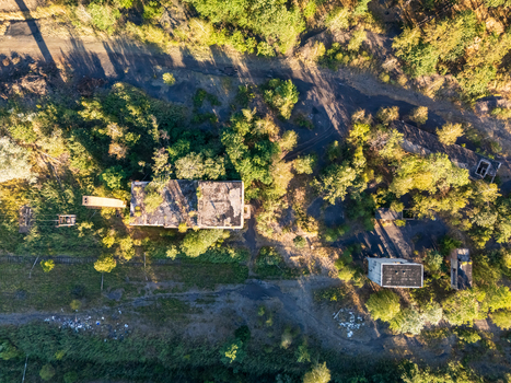 Aerial view of abandoned coal loading facility ruins amid summer forest in Rakoczibanya Hungary showing overgrown industrial buildings rail tracks dirt roads and dark spoil ground. Aerial view of abandoned coal loading facility ruins amid summer forest in Rakoczibanya Hungary showing overgrown industrial buildings rail tracks dirt roads and dark spoil ground.