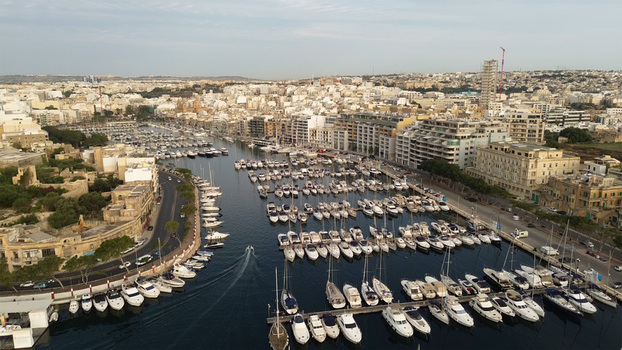 Aerial view of the marina in Msida with numerous yachts and boats docked along the waterfront surrounded by urban architecture and historic buildings in Malta. Aerial view of the marina in Msida with numerous yachts and boats docked along the waterfront surrounded by urban architecture and historic buildings in Malta.