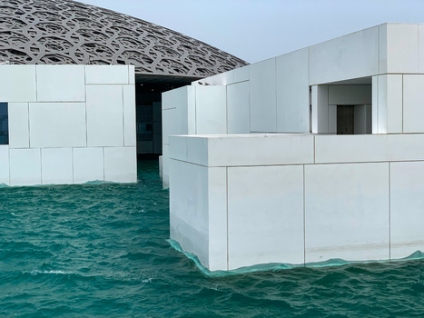 View of modern white geometric structures and a large patterned dome of a Louvre museum Abu Dhabi over turquoise water in Abu Dhabi Abu Dhabi United Arab Emirates. View of modern white geometric structures and a large patterned dome of a Louvre museum Abu Dhabi over turquoise water in Abu Dhabi Abu Dhabi United Arab Emirates.