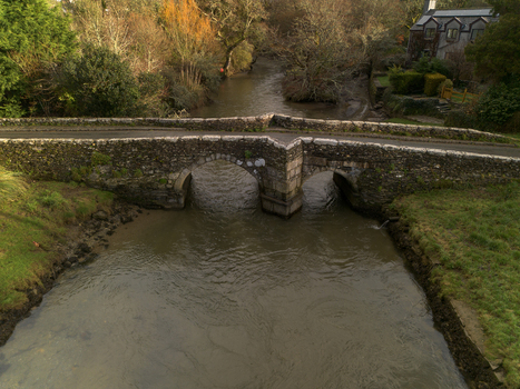 Aerial view of the historic stone bridge spanning the River Lerryn surrounded by lush trees and greenery in the countryside of Lerryn Cornwall United Kingdom. Aerial view of the historic stone bridge spanning the River Lerryn surrounded by lush trees and greenery in the countryside of Lerryn Cornwall United Kingdom.
