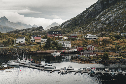 Sund Nordland Norway 04 September 2025 View of the coastal village of Sund with colorful houses a harbor filled with boats and dramatic mountains under a cloudy sky.