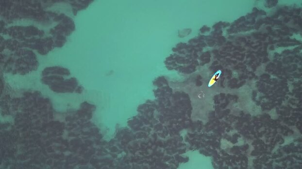 Aerial view of paddleboarder over rocky seabed in Spain.