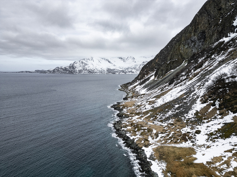 Aerial view of Grotfjord with snow covered mountains rocky coastline and dark sea under a cloudy sky in Tromvik Troms Norway. Aerial view of Grotfjord with snow covered mountains rocky coastline and dark sea under a cloudy sky in Tromvik Troms Norway.
