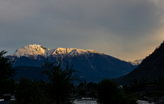 View of snow capped mountains of Kumrat Valley illuminated by golden hour light under a dramatic cloudy sky in Kumrat Valley Khyber Pakhtunkhwa Pakistan. View of snow capped mountains of Kumrat Valley illuminated by golden hour light under a dramatic cloudy sky in Kumrat Valley Khyber Pakhtunkhwa Pakistan.