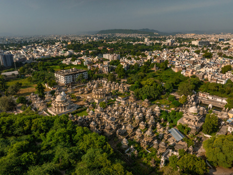 Aerial view of the historic Ahar Cenotaphs with numerous white marble domes nestled among lush green trees set against the backdrop of the urban landscape in Udaipur Rajasthan India.