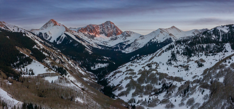 Aerial view of Capitol Peak in the Rocky Mountains during a winter sunset featuring snow covered slopes and evergreen forests in Aspen Colorado United States.
