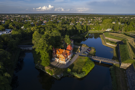 Aerial view of Kuressaare Castle with its distinctive red roof surrounded by a calm moat and lush green trees with the town of Kuressaare in the background Kuressaare Saare County Estonia.