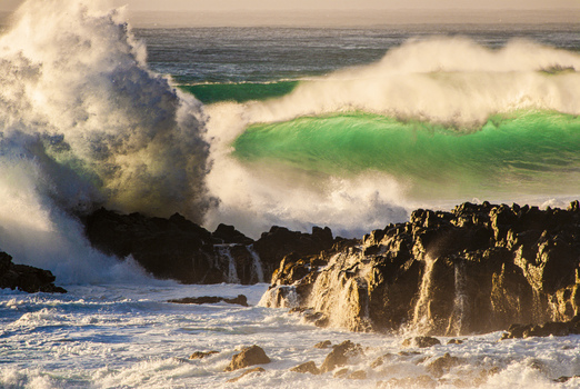View of powerful waves crashing against the dark volcanic rocks of the North Shore at sunset in Haleiwa Hawaii United States.