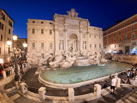 View of the Trevi Fountain at night illuminated by warm lights with people gathered around the historic baroque sculpture and water basin in Roma Lazio Italy.