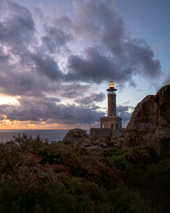 View of Faro de Punta Nariga lighthouse standing on a rocky coastline under a dramatic sunset sky with heavy clouds over the Atlantic Ocean Malpica A Coruna Spain. View of Faro de Punta Nariga lighthouse standing on a rocky coastline under a dramatic sunset sky with heavy clouds over the Atlantic Ocean Malpica A Coruna Spain.