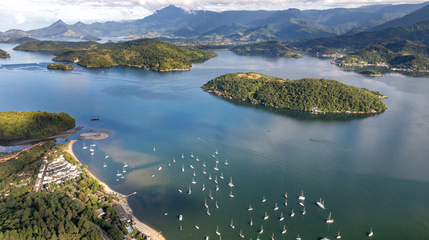 Aerial view of numerous sailboats anchored in the calm blue bay surrounded by lush green islands and coastal mountains in Angra dos Reis Rio de Janeiro Brazil.