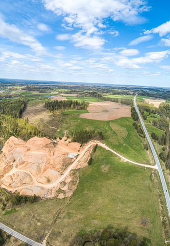 Aerial view of a gravel pit with sandy mounds surrounded by green fields forest patches and a long road stretching through the rural landscape of Latvia. Aerial view of a gravel pit with sandy mounds surrounded by green fields forest patches and a long road stretching through the rural landscape of Latvia.