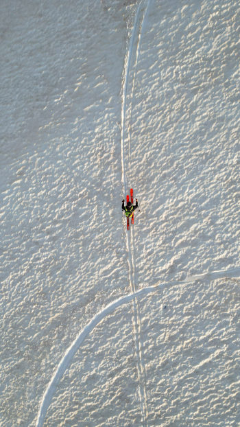Aerial view of a skier with orange skis moving across a textured snow covered slope near Le Colomby de Gex in Echenevex Auvergne Rhone Alpes France. Aerial view of a skier with orange skis moving across a textured snow covered slope near Le Colomby de Gex in Echenevex Auvergne Rhone Alpes France.