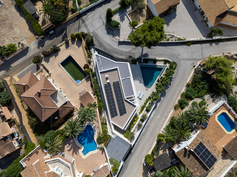 Aerial view of modern villas with swimming pools and solar panels surrounded by palm trees and winding roads in Moraira Valencian Community Spain.
