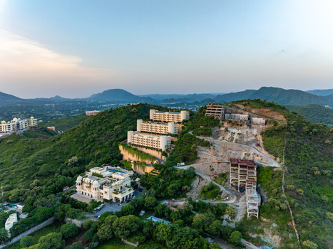 Aerial view of a luxury resort complex with tiered buildings and lush greenery situated on a hillside in Udaipur Rajasthan India.