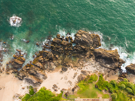 Aerial view of a rocky coastline with turquoise ocean waves crashing against stone formations and a sandy beach in Galle Southern Province Sri Lanka.