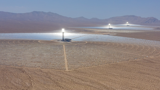 Aerial view of a large concentrated solar power plant with thousands of heliostat mirrors arranged in circular patterns around central receiver towers in a desert landscape United States.