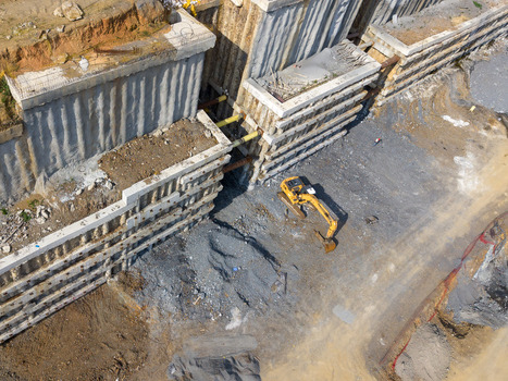 Aerial view of a construction site with a yellow excavator working near a deep excavation pit supported by concrete retaining walls and metal struts in Istanbul Istanbul Turkiye.