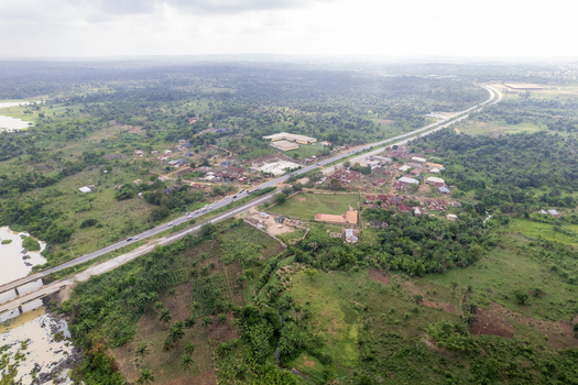Aerial view of a long road cutting through lush green landscape a bridge over a river buildings and abundant trees Asejire Oyo Nigeria. Aerial view of a long road cutting through lush green landscape a bridge over a river buildings and abundant trees Asejire Oyo Nigeria.