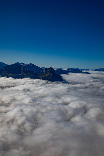 Aerial view of the Swiss Alps rising above a thick layer of clouds under a clear blue sky in Airolo Ticino Switzerland. Aerial view of the Swiss Alps rising above a thick layer of clouds under a clear blue sky in Airolo Ticino Switzerland.