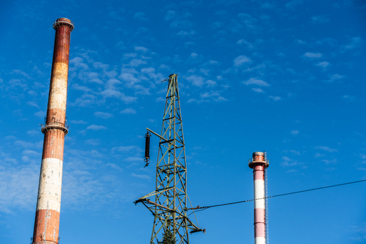 View of industrial chimneys and a power transmission tower standing against a clear blue sky in Poland.