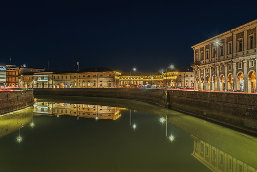 View of the illuminated historic buildings and Portici Ercolani reflected in the Misa River at night in Senigallia Marche Italy.