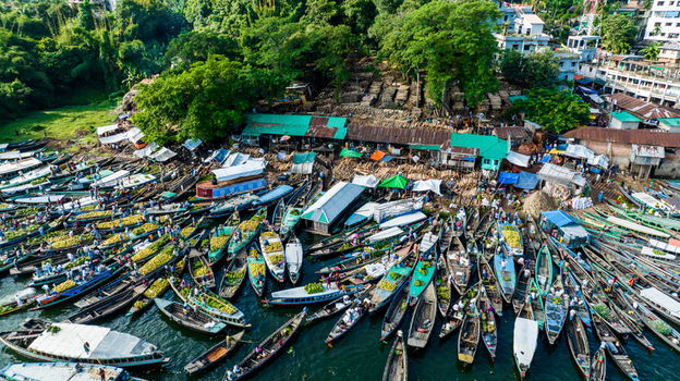 Rangamati Bangladesh 19 October 2022 Aerial view of the bustling boat market with numerous wooden boats laden with goods docked along the shore surrounded by lush trees.