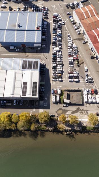 Aerial view of a parking lot with many cars adjacent to industrial buildings with solar panels situated along a riverbank with trees in Zumaia Basque Country Spain.