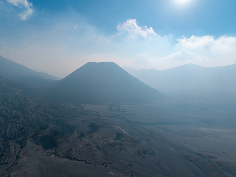 Aerial view of Mount Bromo volcano rising from the vast volcanic sand sea with hazy atmosphere and bright sunlight in Tosari East Java Indonesia.