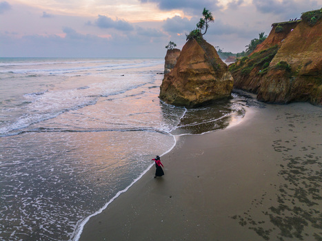 Aerial view of a person walking along the sandy beach near dramatic rock formations and cliffs at sunset in Bali Indonesia. Aerial view of a person walking along the sandy beach near dramatic rock formations and cliffs at sunset in Bali Indonesia.