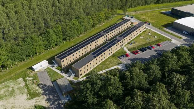 Aerial view of a long modern building complex with solar panels on the roof adjacent to a parking lot and surrounded by trees in Middenmeer North Holland Netherlands.