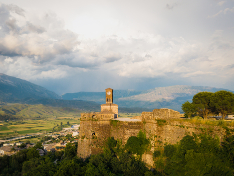 Aerial view of the historic Gjirokaster Fortress featuring its iconic clock tower and ancient stone walls overlooking the valley and mountains in Gjirokaster Gjirokaster County Albania. Aerial view of the historic Gjirokaster Fortress featuring its iconic clock tower and ancient stone walls overlooking the valley and mountains in Gjirokaster Gjirokaster County Albania.