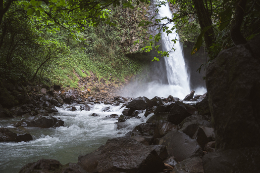 View of a powerful waterfall cascading into a rocky stream surrounded by lush tropical jungle foliage in Costa Rica.