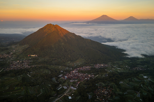 Aerial view of Mount Andong rising above a sea of clouds at sunrise with terraced fields and village houses nestled in the landscape of Ngablak Central Java Indonesia.