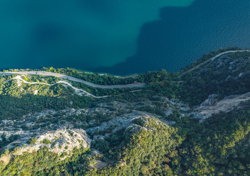 Aerial view of the winding lakeside road along the steep forested cliffs and deep blue water of Lake Garda Italy.