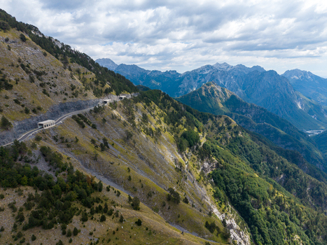 Aerial view of the Albanian Alps with a winding mountain road and tunnels carved into rocky slopes surrounded by forests and rugged peaks in Shkoder Shkoder County Albania. Aerial view of the Albanian Alps with a winding mountain road and tunnels carved into rocky slopes surrounded by forests and rugged peaks in Shkoder Shkoder County Albania.