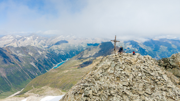 Aerial view of Grosser Moseler summit with hikers near the wooden cross overlooking rocky terrain and a turquoise reservoir in the valley in Schwaz District Tyrol Austria. Aerial view of Grosser Moseler summit with hikers near the wooden cross overlooking rocky terrain and a turquoise reservoir in the valley in Schwaz District Tyrol Austria.
