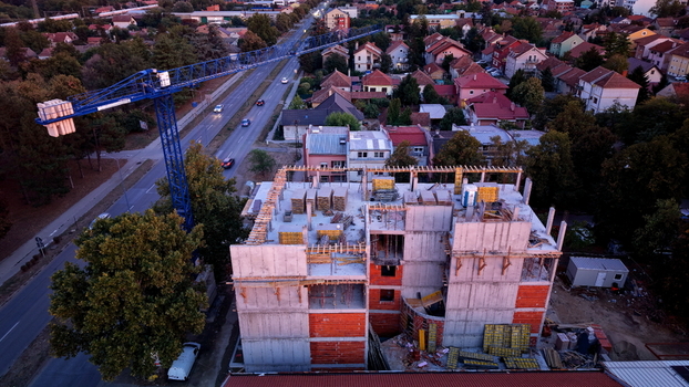 Aerial view of a construction site featuring a blue tower crane concrete structure and brick walls situated near a road with residential houses in Pancevo Vojvodina Serbia.