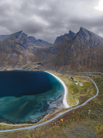 Aerial view of the dramatic coastal landscape of Senja with steep mountains a turquoise bay a sandy beach and a winding road in Senja Troms Norway.