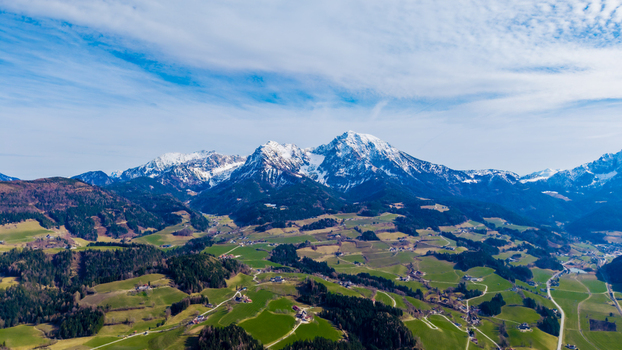 Aerial view of snow capped mountains rise majestically over the lush green valley creating a stunning contrast against the bright blue sky Windischgarsten Upper Austria Austria. Aerial view of snow capped mountains rise majestically over the lush green valley creating a stunning contrast against the bright blue sky Windischgarsten Upper Austria Austria.